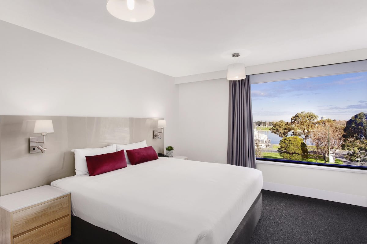 A hotel room with a bed, bedside tables, a nightstand, a window with a view, and a ceiling light.