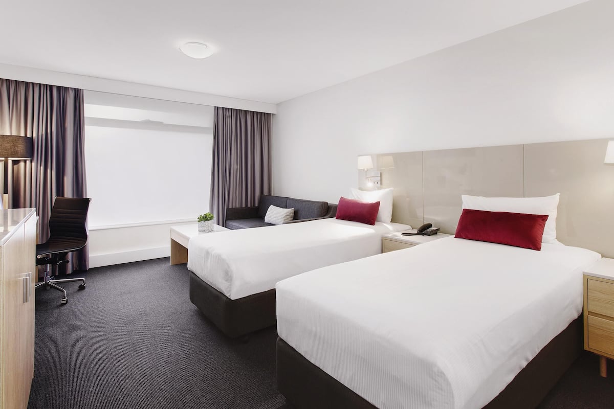 A hotel room with two beds, a desk, a chair, and a window with curtains.
