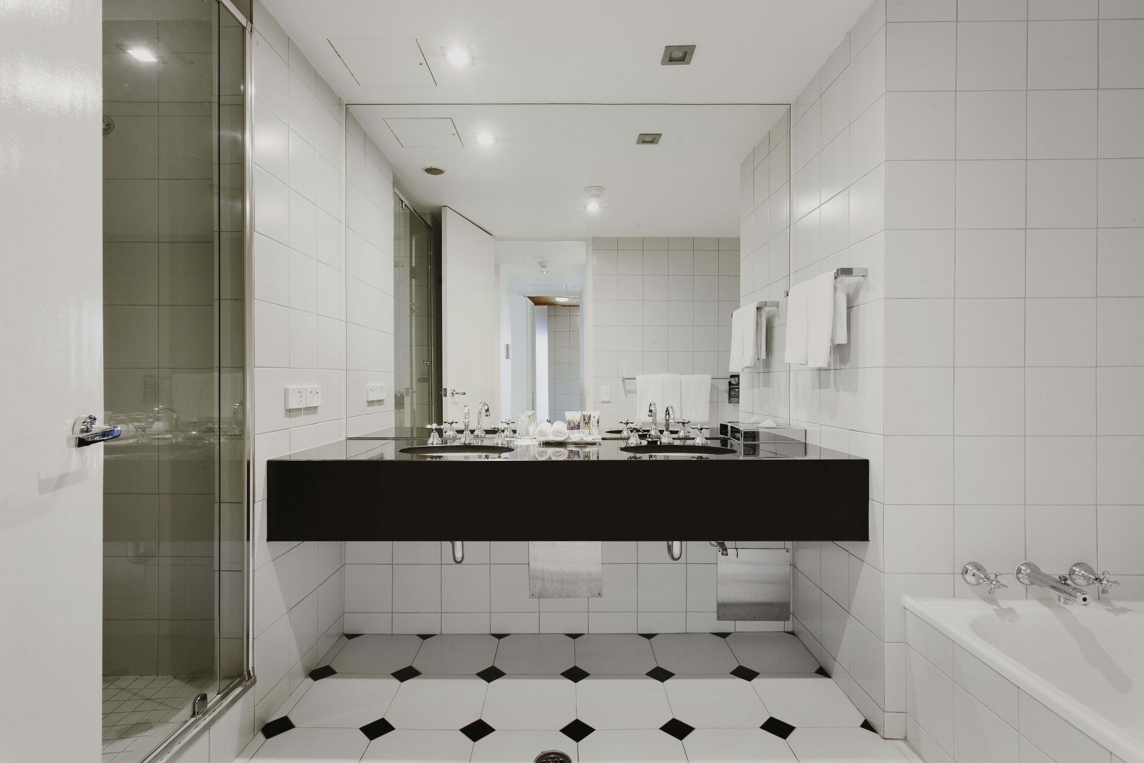 Un baño moderno con encimera negra, azulejos blancos, cabina de ducha de cristal y bañera blanca.