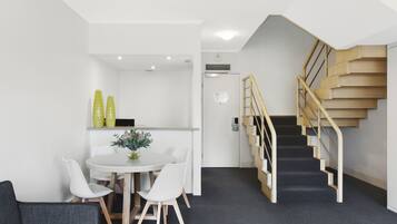 A modern interior with a staircase, a dining area with a table and chairs, and a grey carpeted floor.