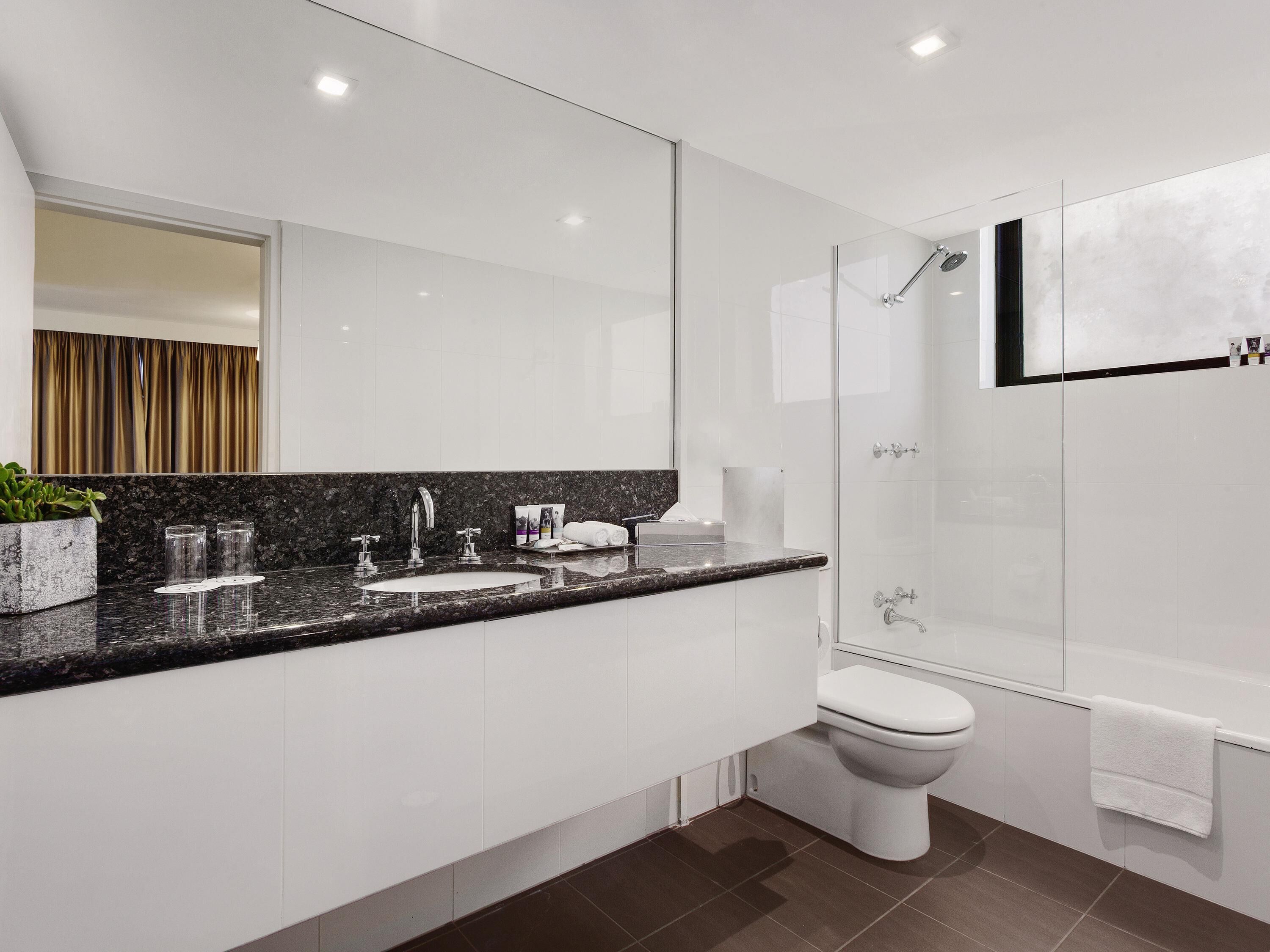 A modern bathroom with a granite countertop, a white sink, a toilet, and a glass-enclosed shower.