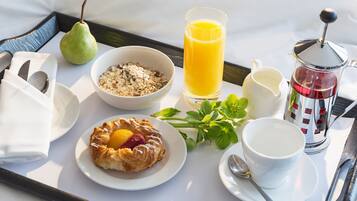 A breakfast tray with a pear, cereal, orange juice, a cup of coffee, a pastry, and a small bowl of milk.