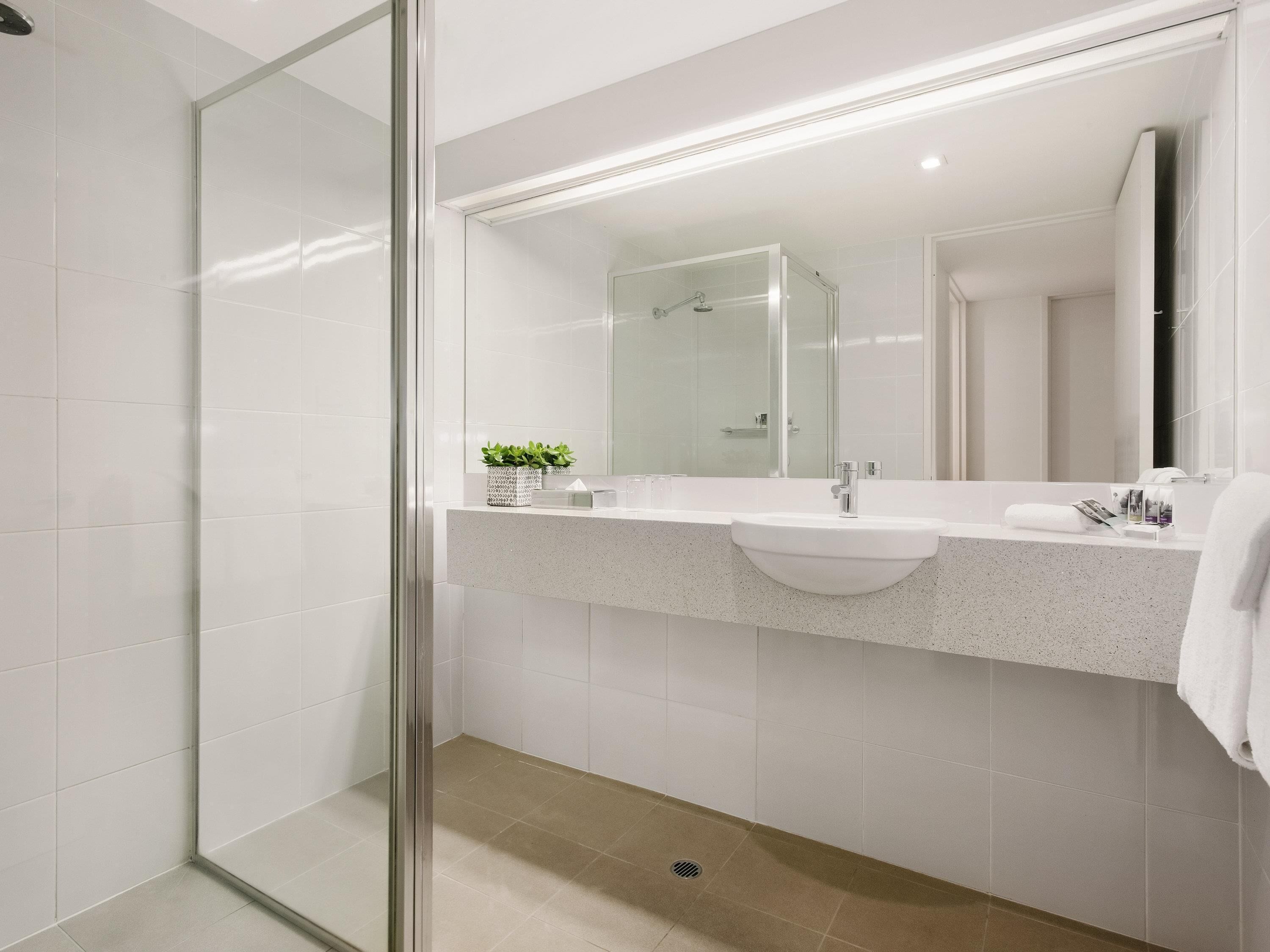A modern bathroom with a glass shower enclosure, a white sink, and a large mirror.