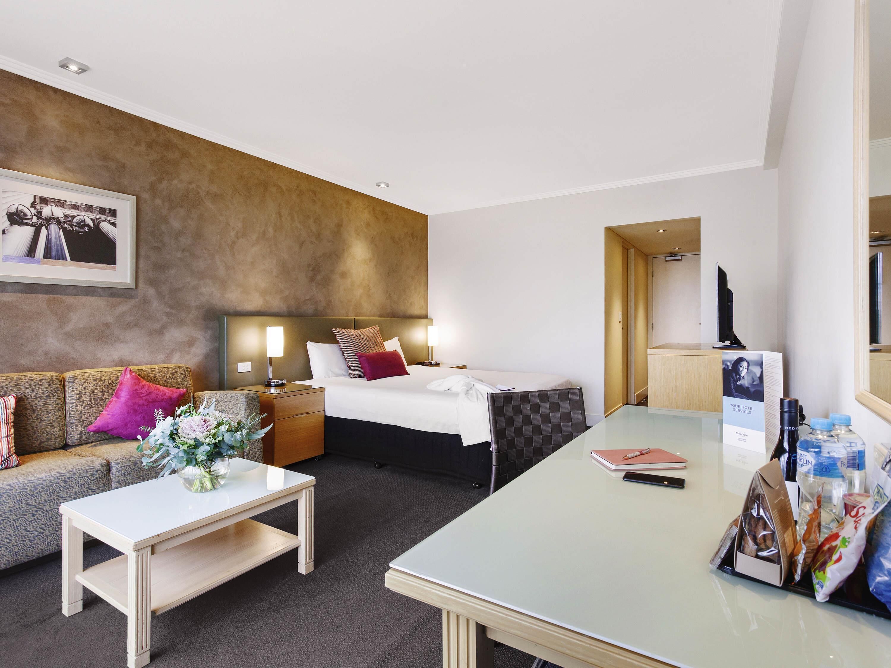 Una habitación de hotel con cama, sofá, mesa de centro, escritorio y televisor.