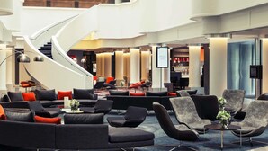 Een moderne lobby met een gebogen trap, zithoeken en een bar.