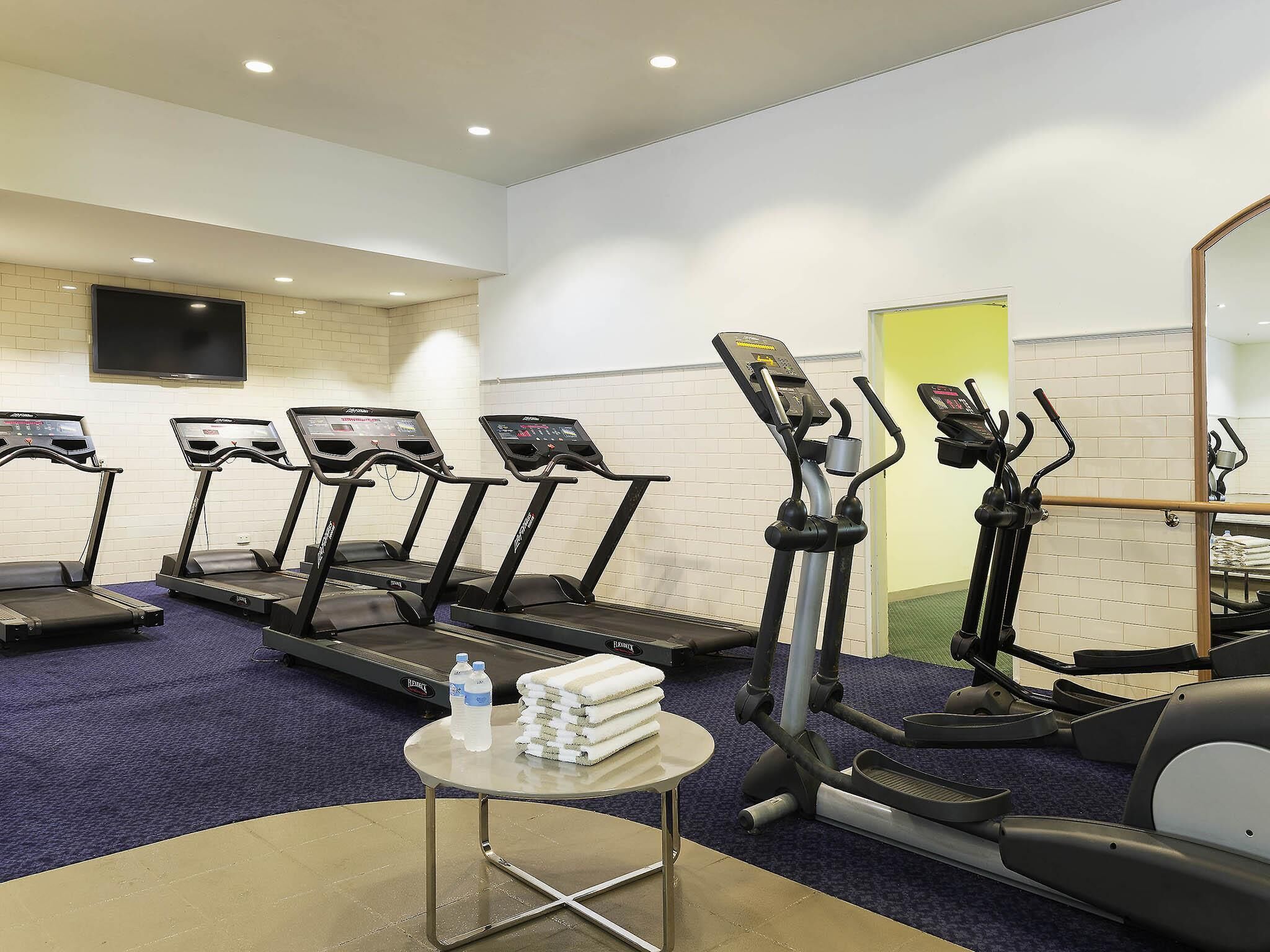 A gym with treadmills, ellipticals, and a mirrored wall.