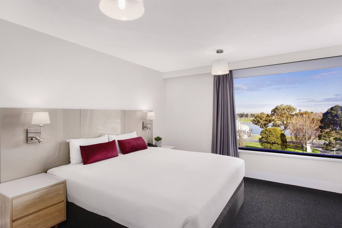 A hotel room with a bed, bedside tables, a nightstand, a window with a view, and a ceiling light.