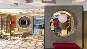 Een moderne hotel lobby met een bank, stoelen, een rode zitbank, een televisie en een ronde spiegel aan de muur.
