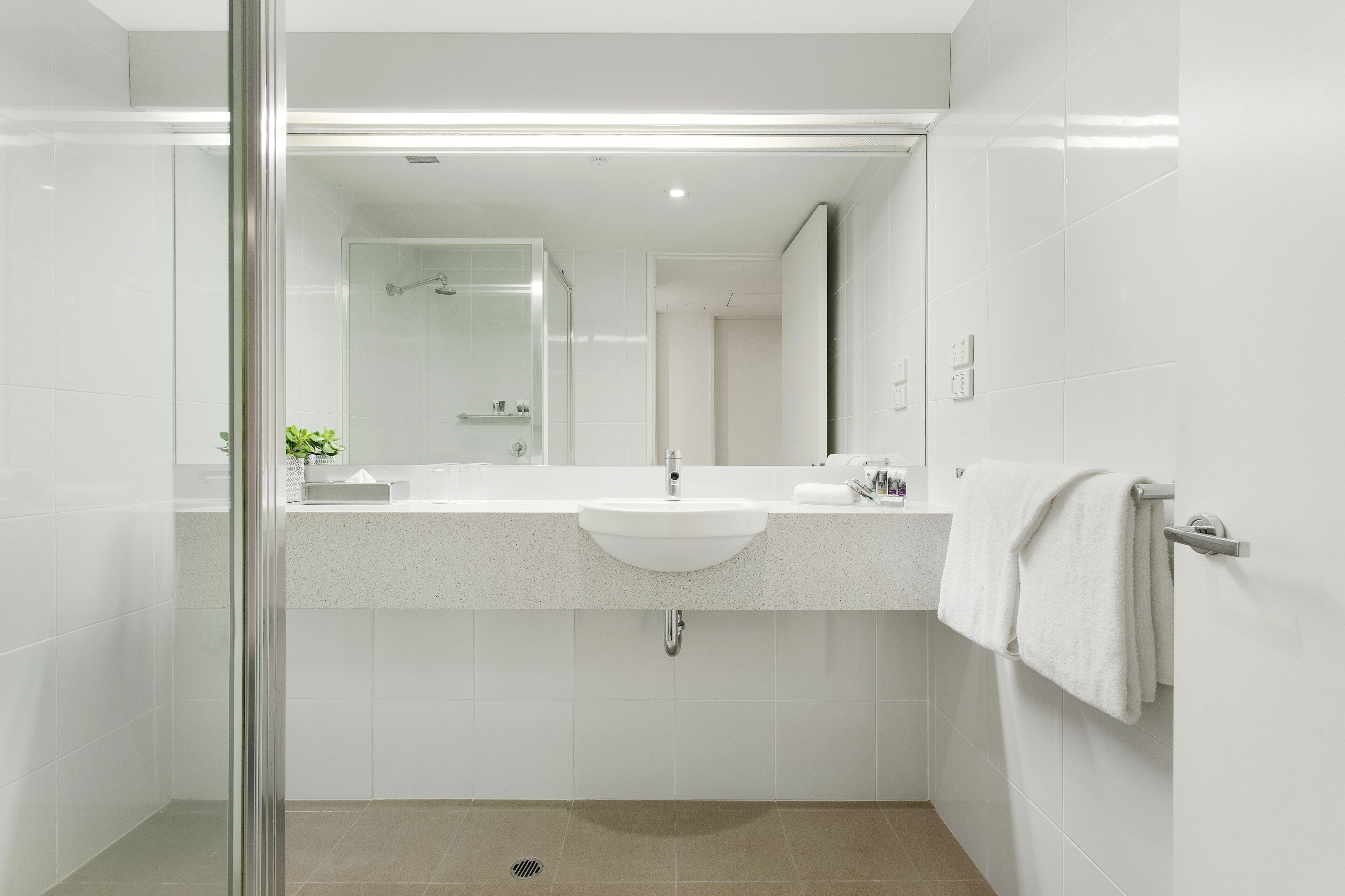 A modern bathroom with a glass shower enclosure, a white sink, and a towel rack.