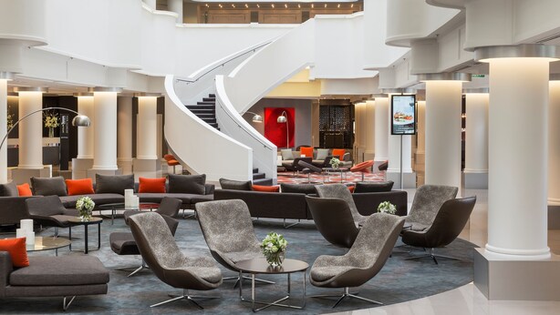Een ruime lobby met een centrale trap, diverse zithoeken en een modern design.