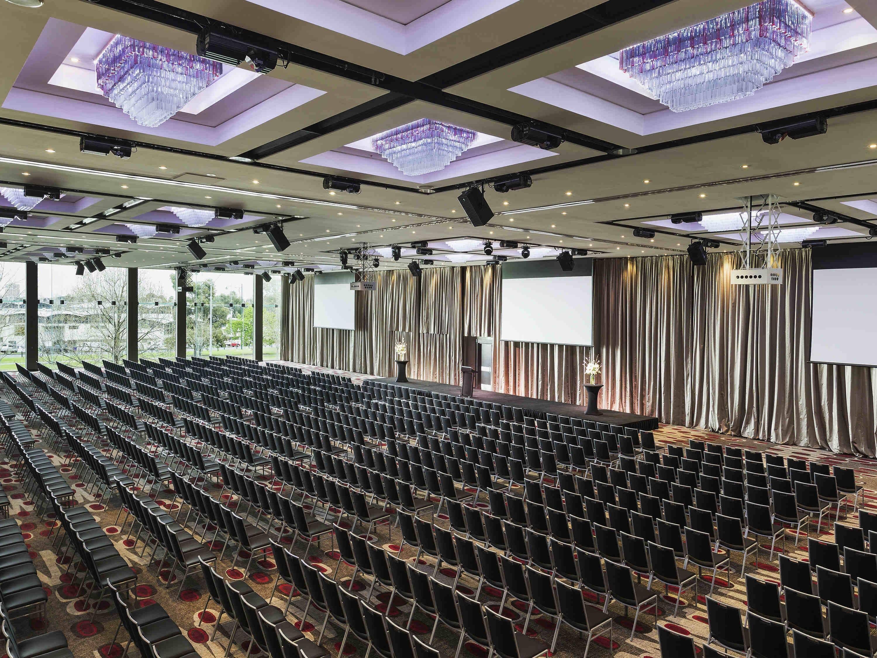 A large auditorium with rows of chairs, a stage with curtains, and a large screen.