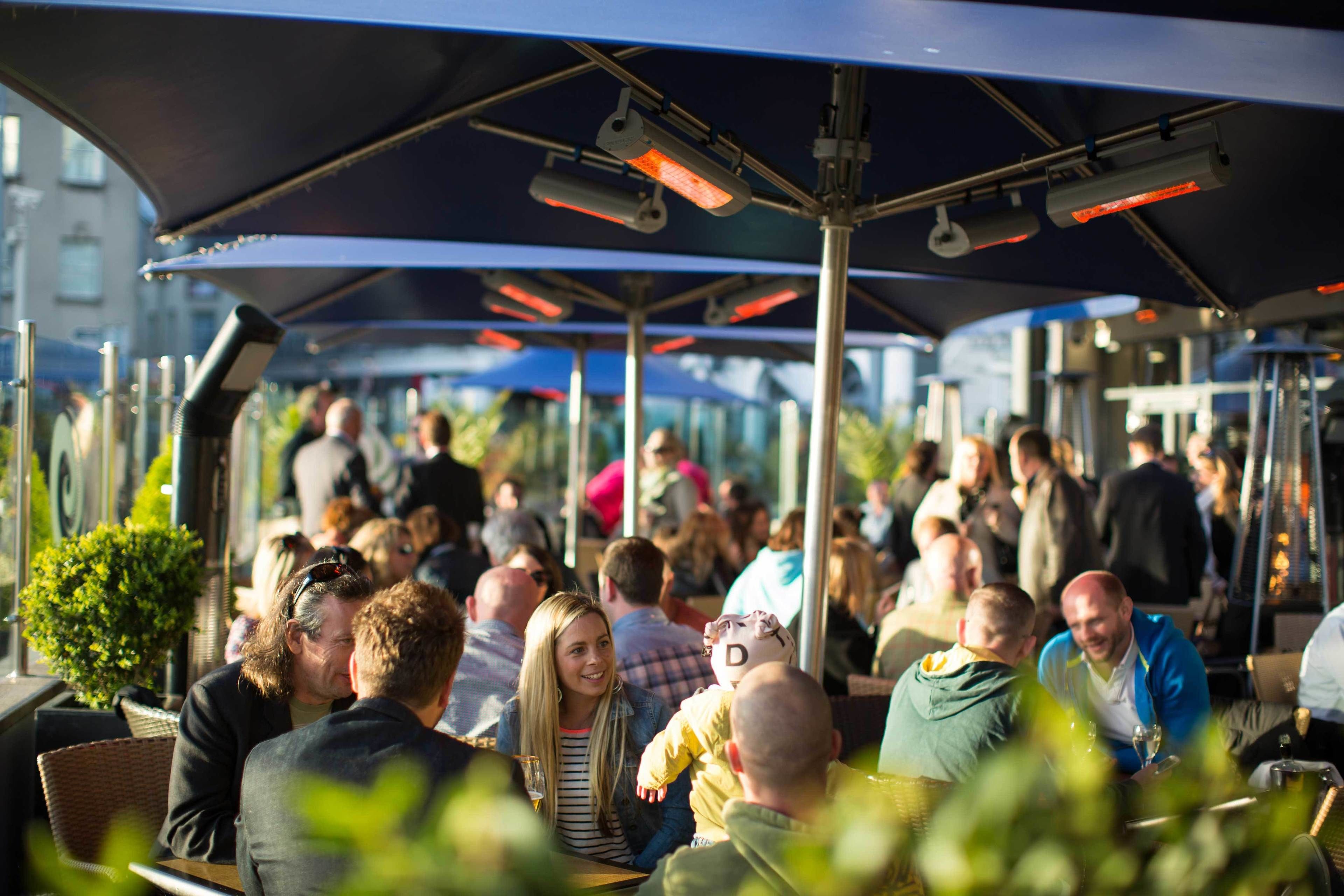 An outdoor seating area with umbrellas and tables, surrounded by people.
