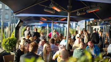 An outdoor seating area with umbrellas and tables, surrounded by people.