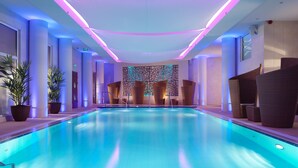 Una piscina interior moderna con una isla central, rodeada de sillones de descanso y plantas en macetas.