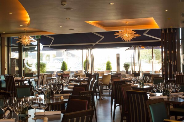Un restaurante con varias mesas y sillas, ventanas amplias y un diseño moderno en el techo.