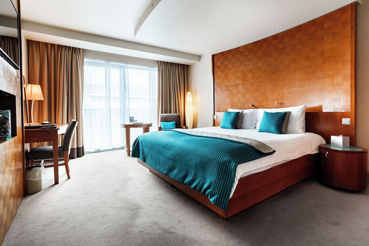 A hotel room with a large bed, a desk, a chair, a lamp, and a nightstand.
