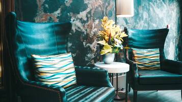 Dos sillones verde oscuro con almohadones a rayas, una mesita redonda con un jarrón de flores amarillas y una pared con textura al fondo.
