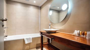 Ein modernes Badezimmer mit Badewanne, einem hölzernen Waschtisch und einem großen Spiegel, sowie einer beige gefliesten Wand.
