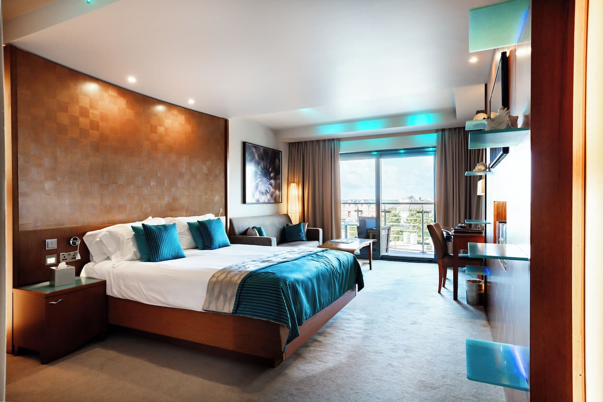 A modern hotel room with a large bed, a desk, and a balcony with a view.