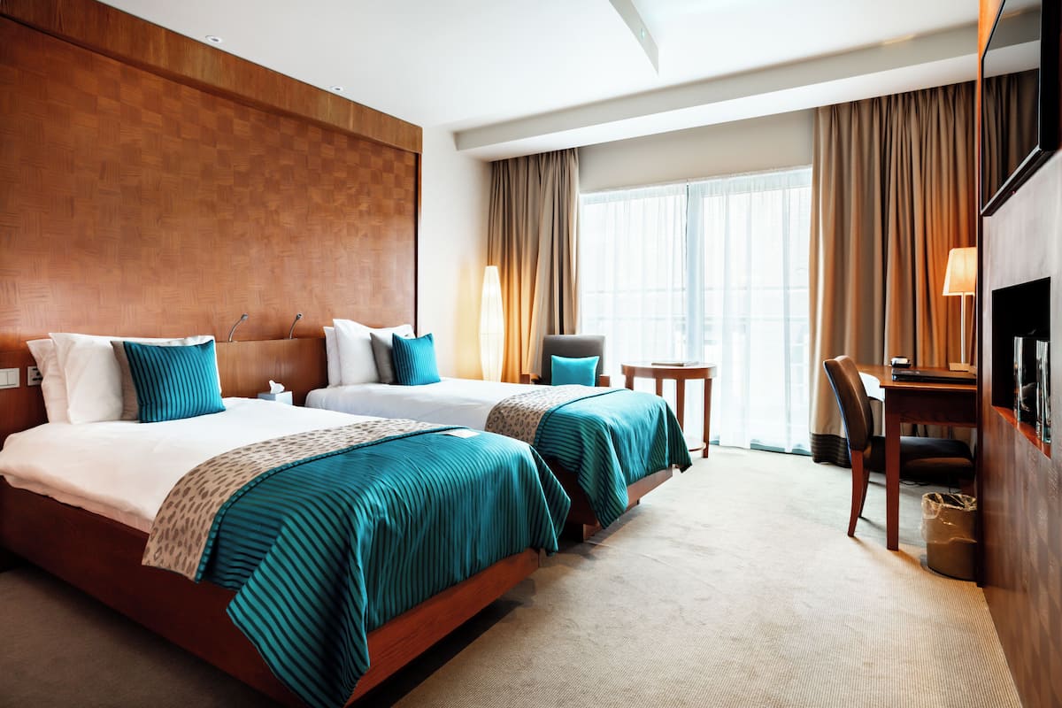 A hotel room with two beds, a desk, a chair, and a TV.