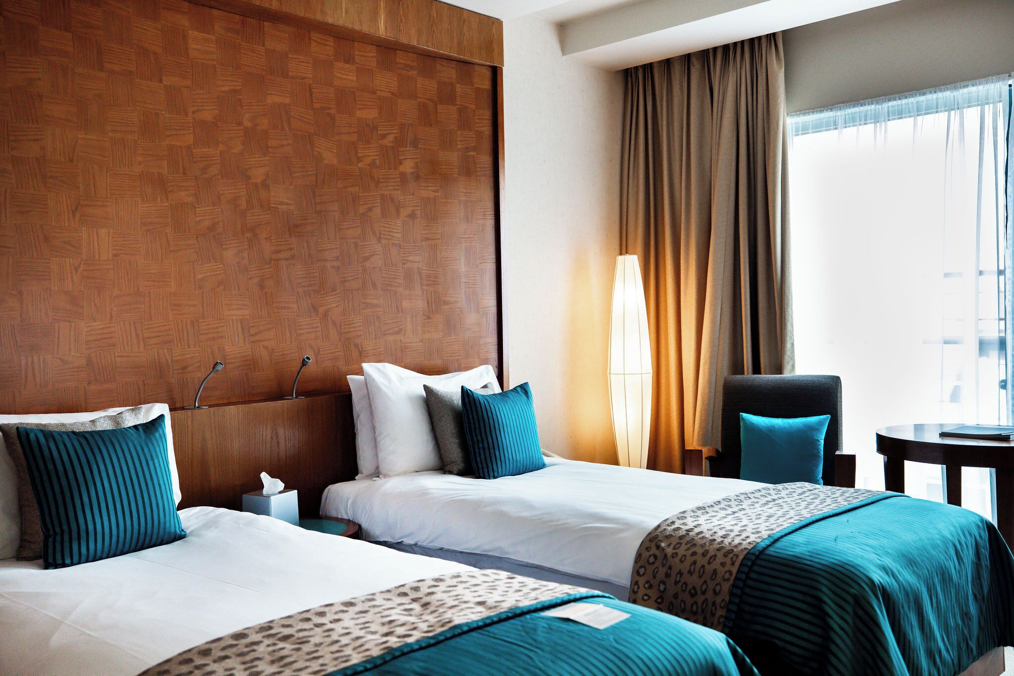 A hotel room with two beds, a wooden headboard, a desk, and a chair.