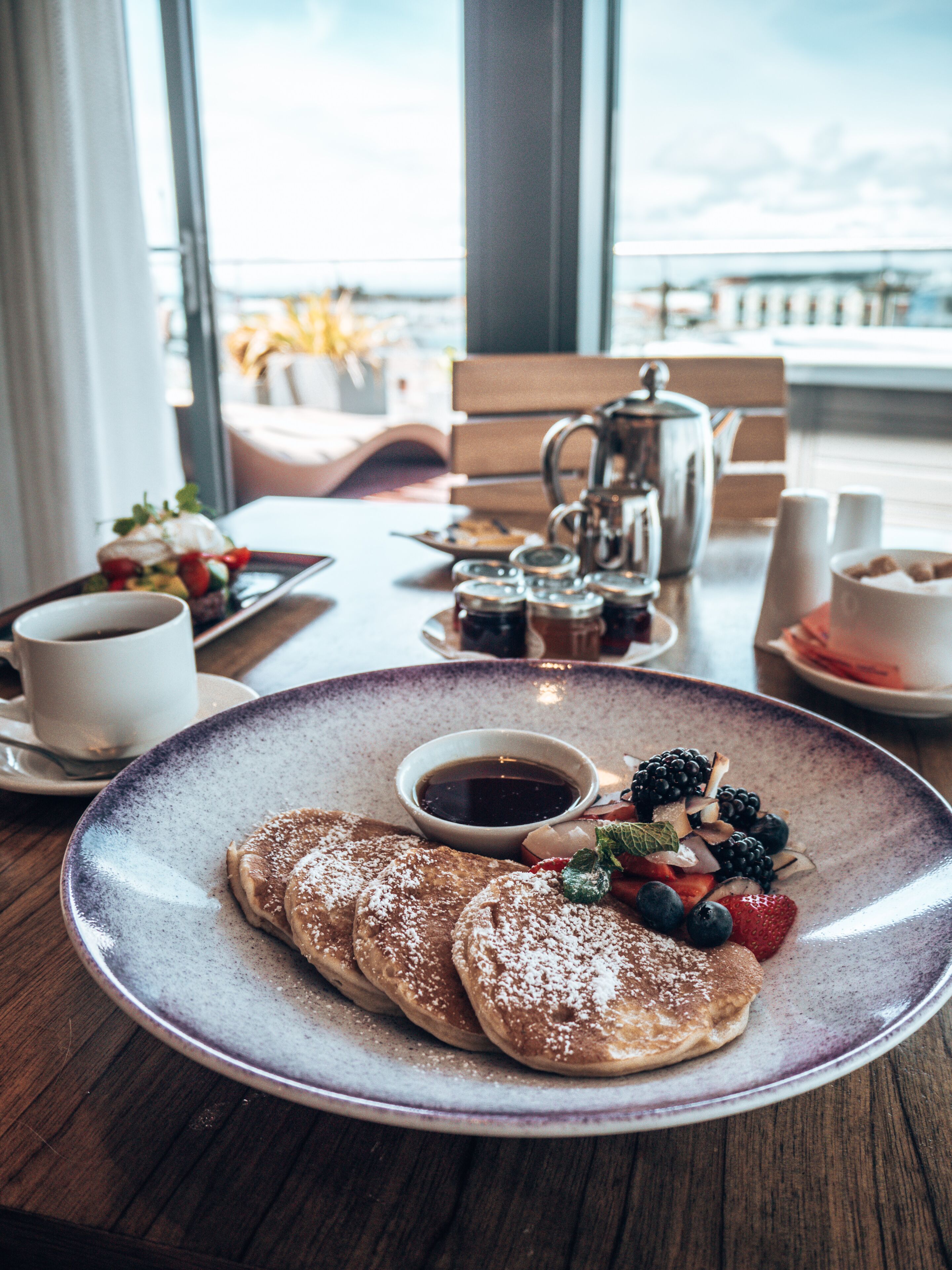 Desayuno con tortitas, frutos rojos y café en un plato.