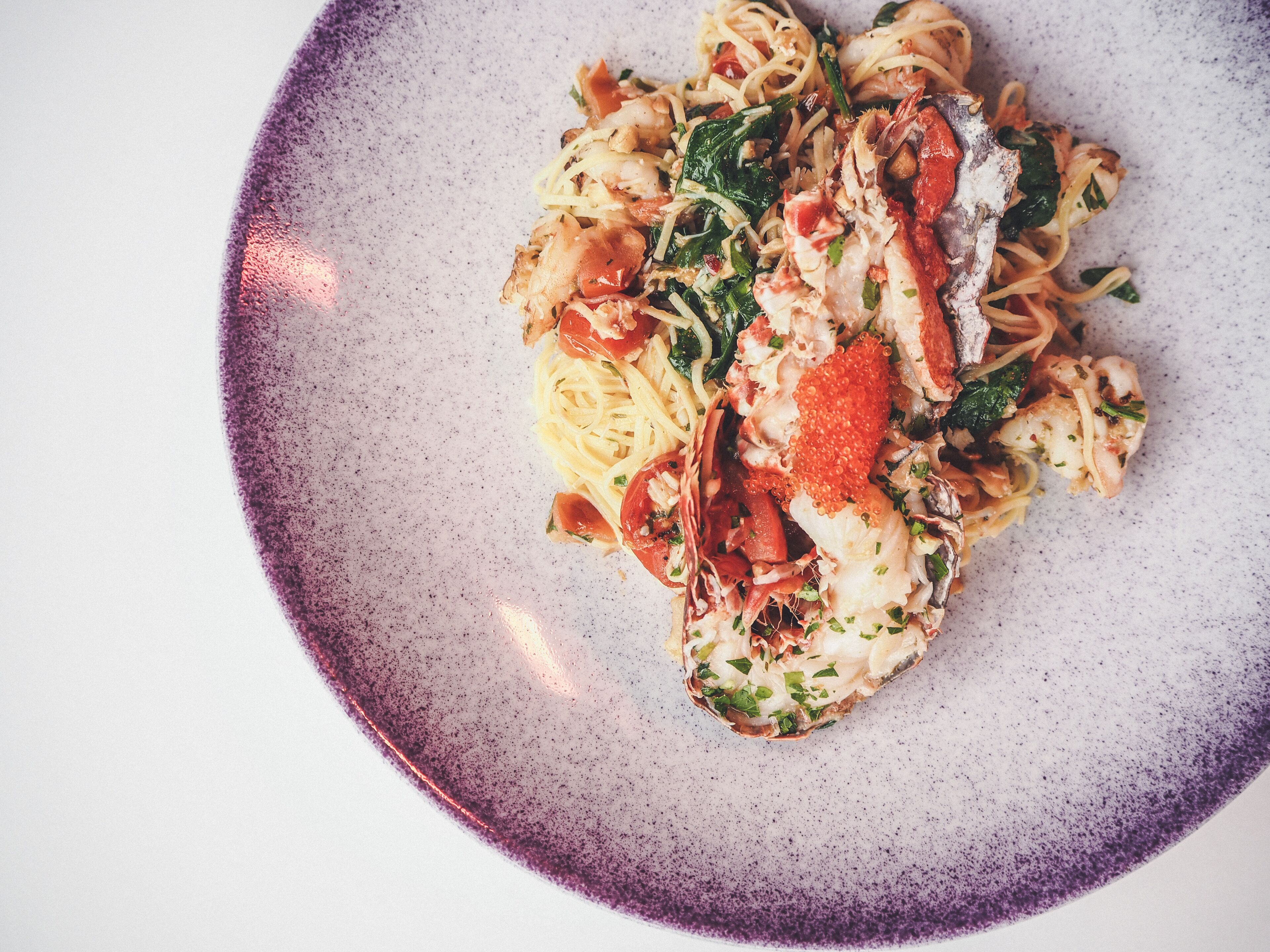 Un plato de pasta con mariscos, incluyendo camarones y langosta, adornado con hierbas.