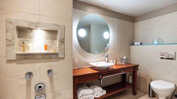 A modern bathroom with a large mirror, a sink, a toilet, and a shelf with toiletries.
