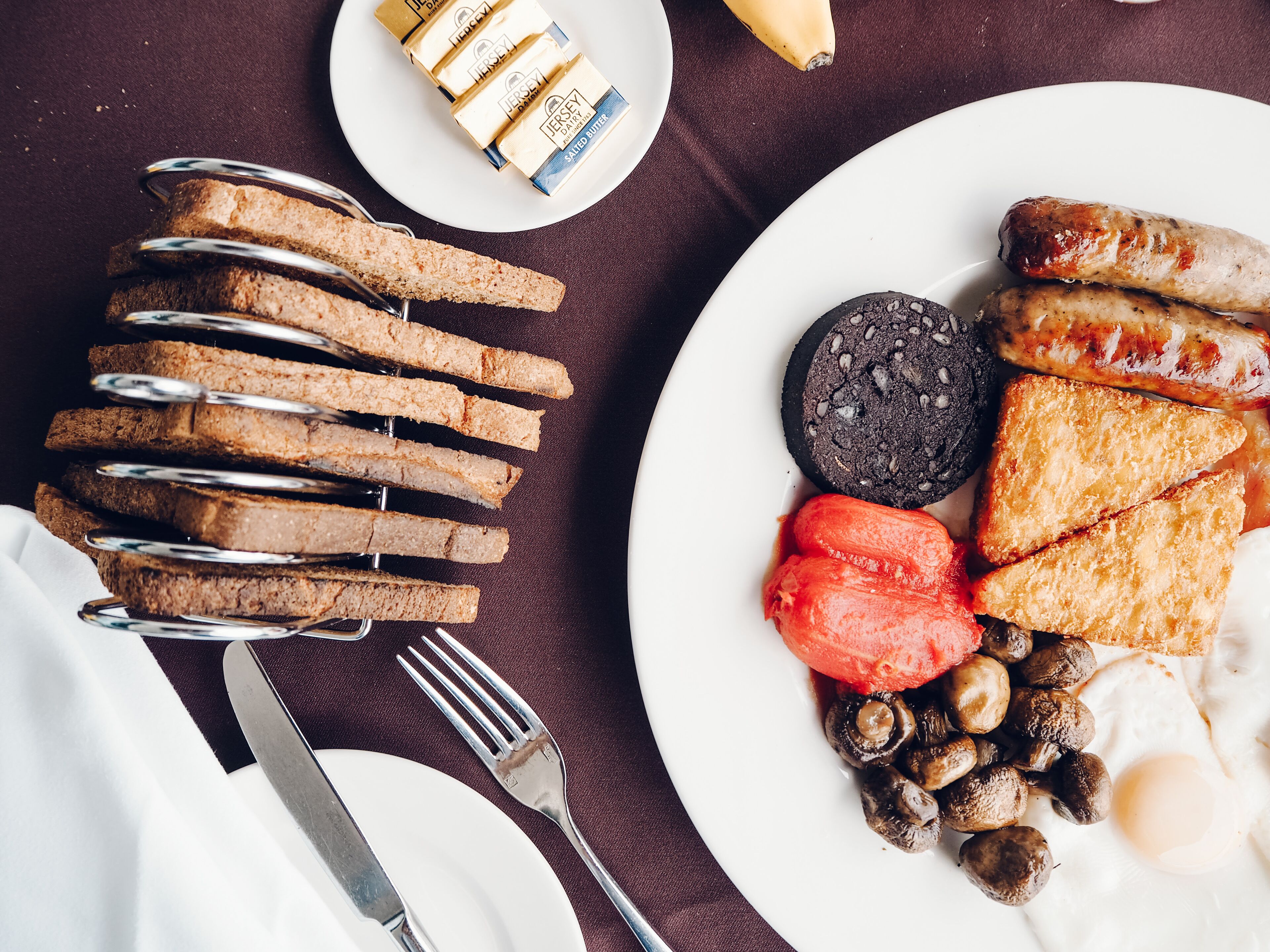 Une assiette de petit-déjeuner comprenant des toasts, des saucisses, des champignons, un œuf au plat et une tranche de boudin noir.