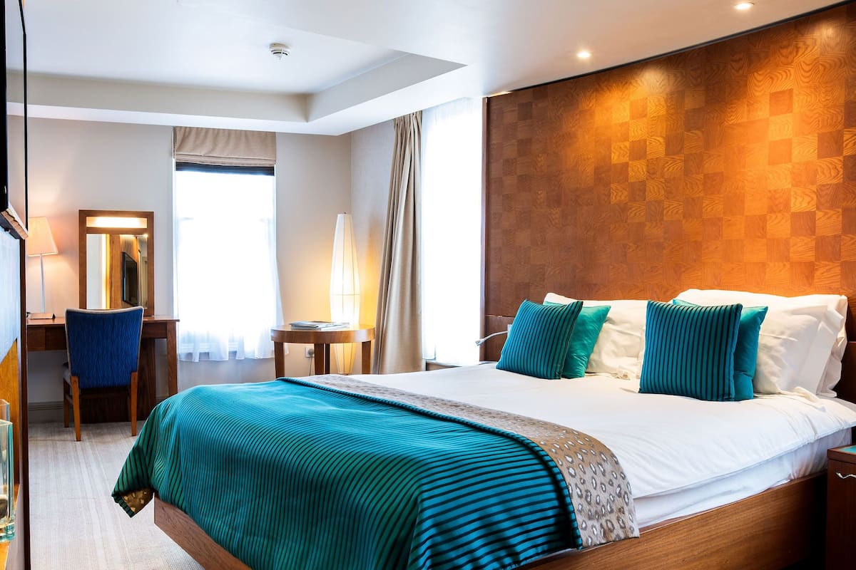A hotel room with a large bed, a desk, a chair, and a lamp.