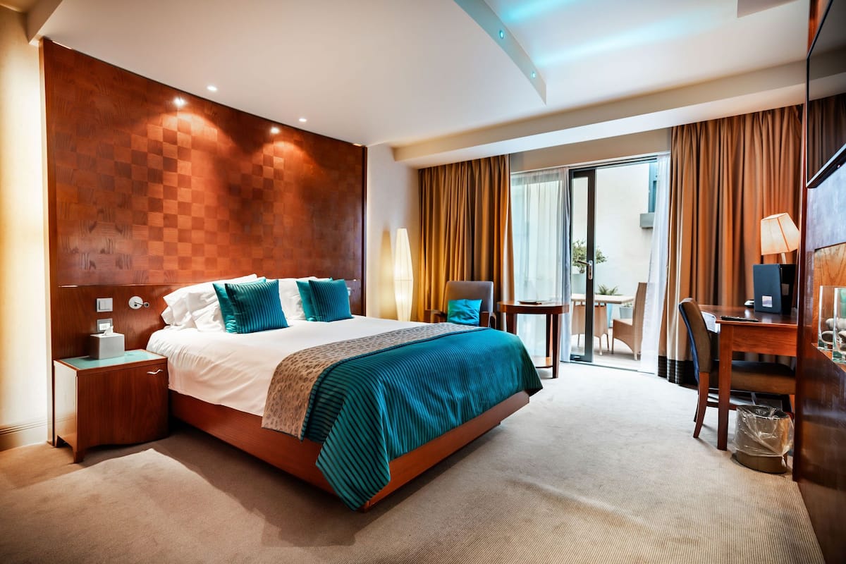 A hotel room with a large bed, a wooden headboard, a desk with a chair, and a view of the outside.