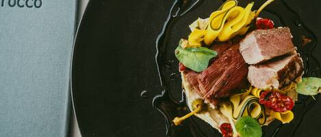 A black plate with a dish of food, including meat and vegetables, on a table.
