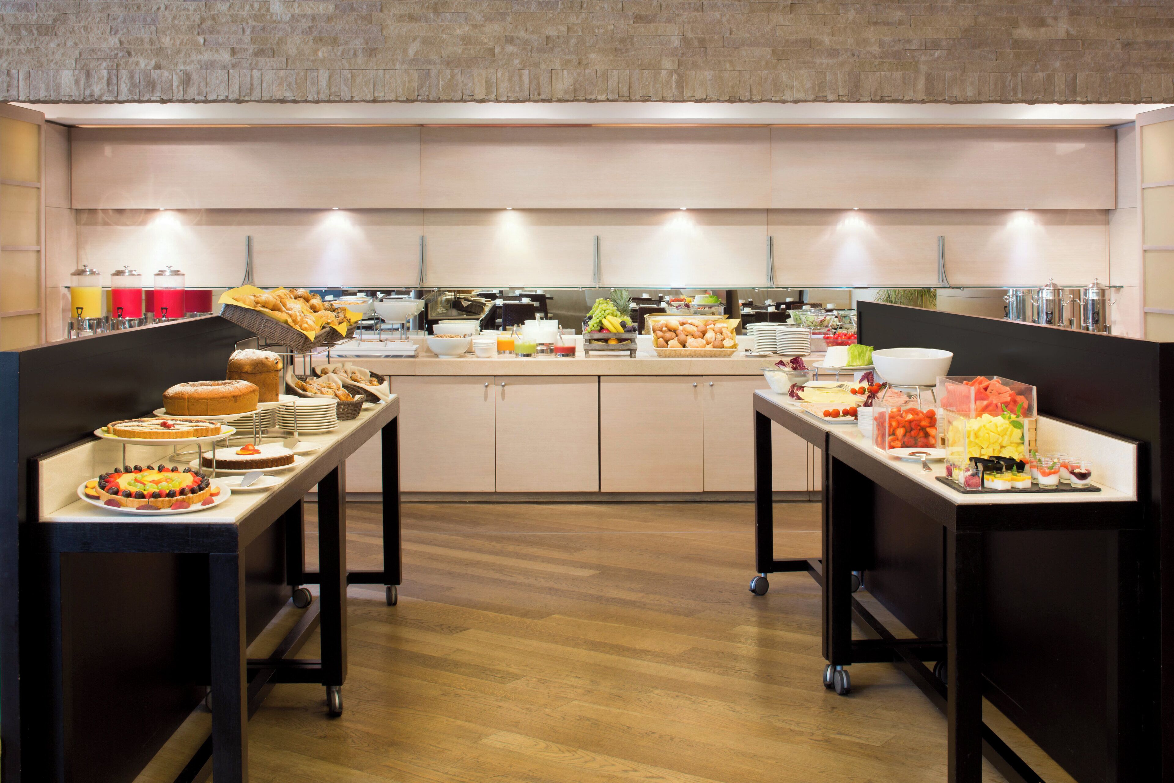 Un buffet proposant une variété de plats et de boissons, notamment des fruits, des pâtisseries et des salades, disposés sur des tables et des comptoirs.
