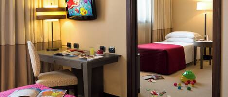 Habitación de hotel con cama, escritorio con silla, televisor y juguetes en el suelo.