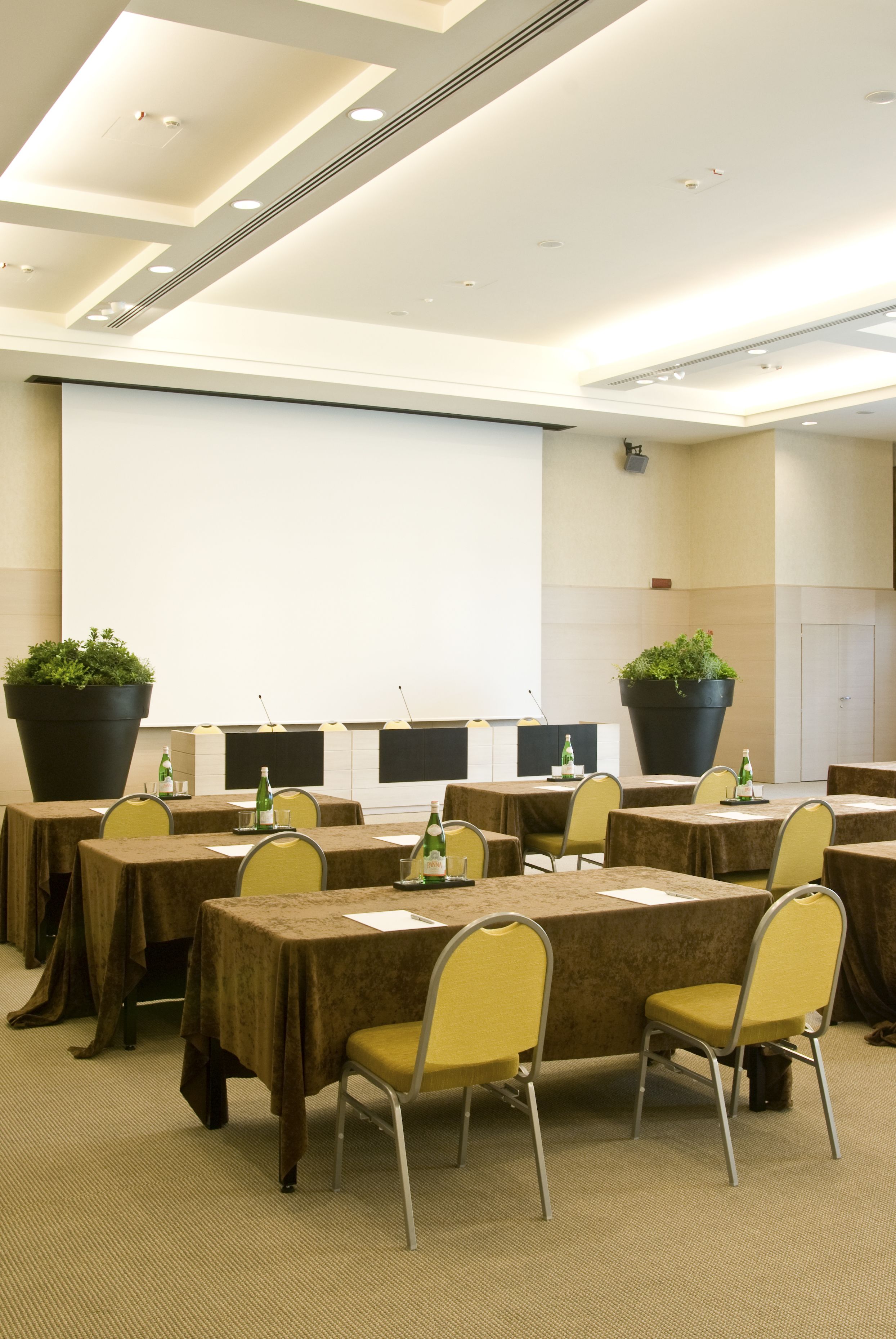 A conference room with tables, chairs, and large potted plants.