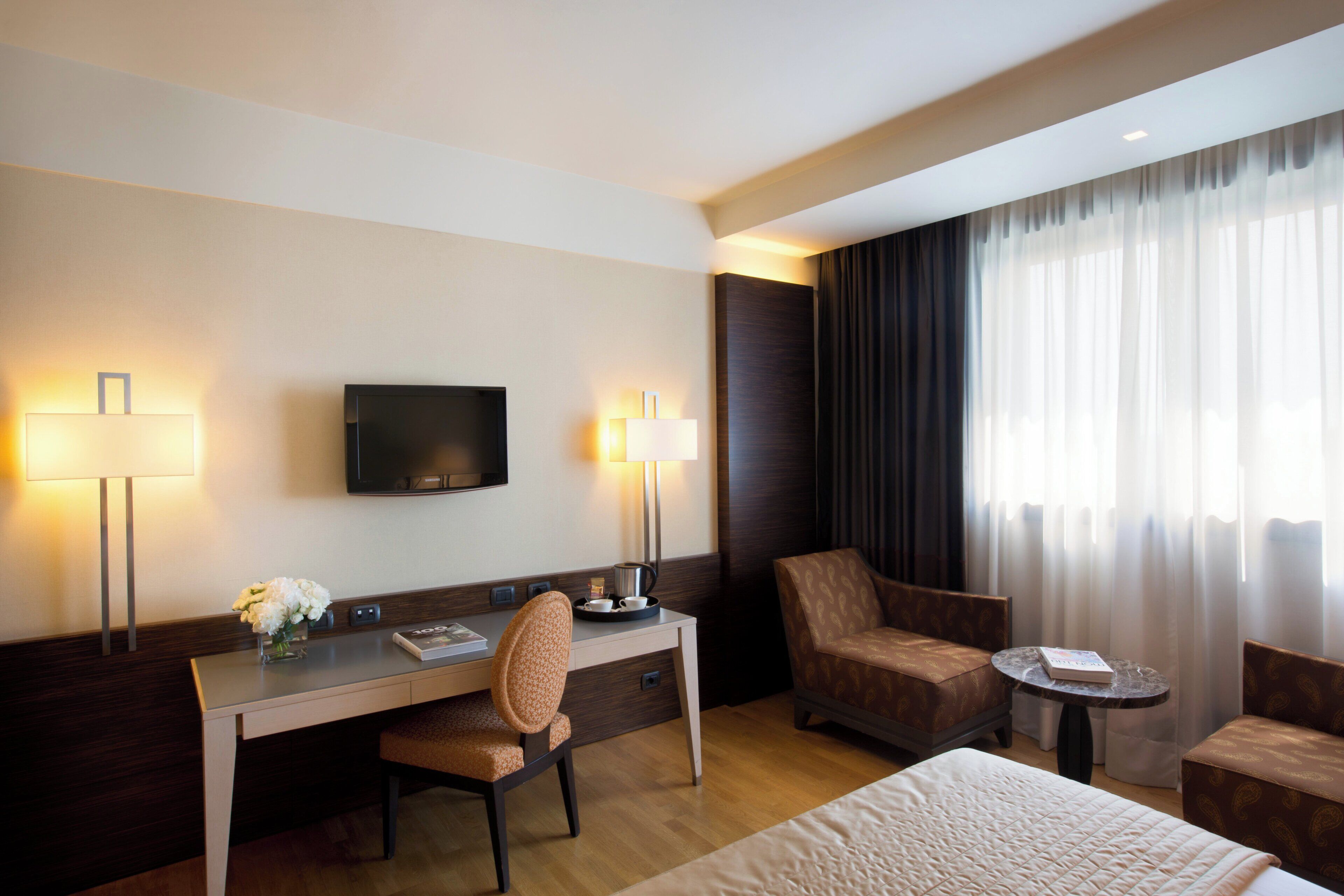 Une chambre d’hôtel avec un lit, un bureau, une chaise, une télévision et une fenêtre avec des rideaux.