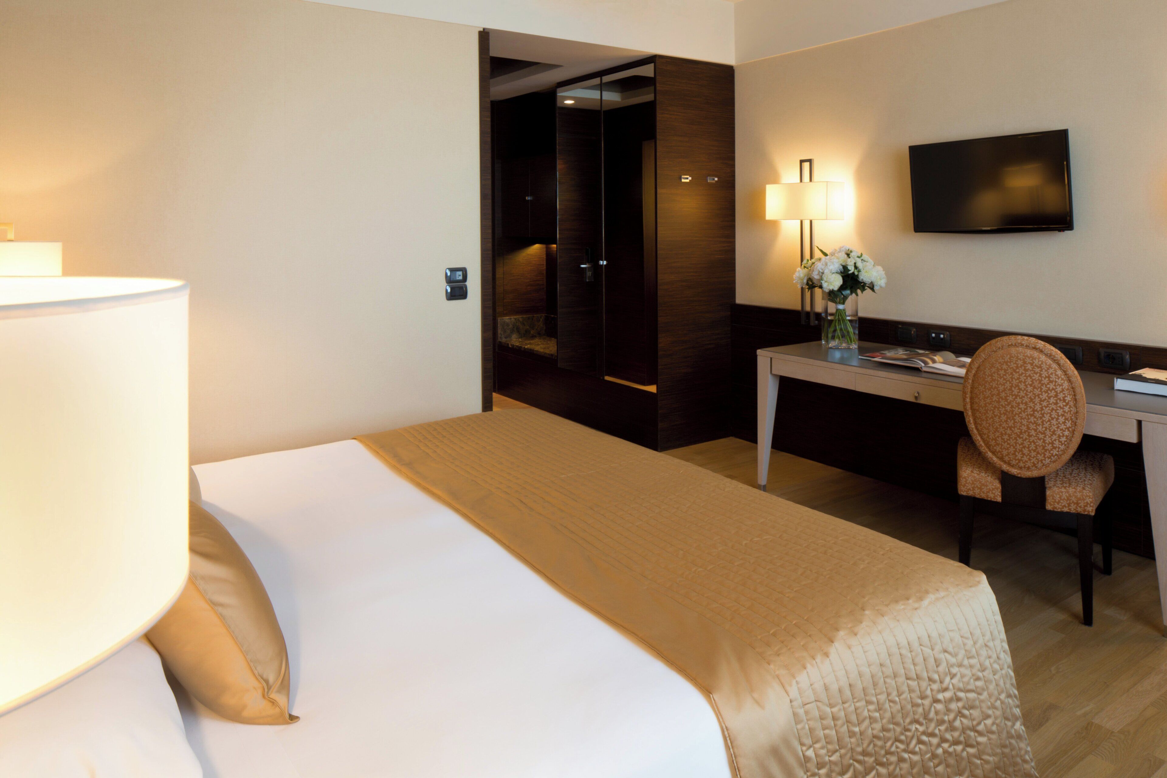 A hotel room with a bed, a desk, a chair, a television, and a lamp.