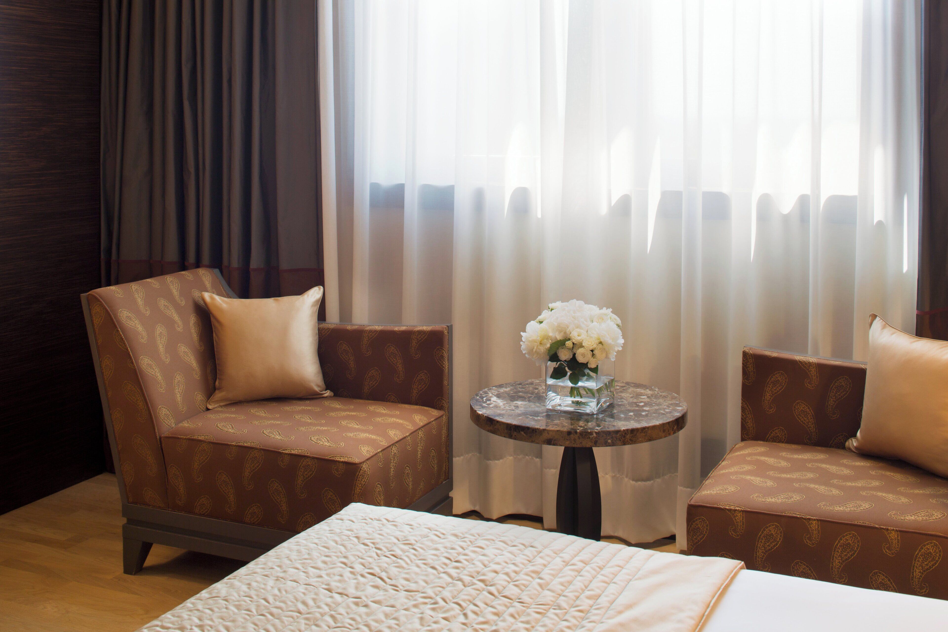 Hotelkamer met een bed, twee slaapbanken, een kleine tafel met een bloevas en uitzicht door dunne gordijnen.