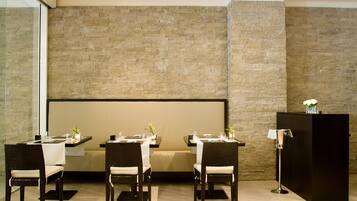 Un comedor moderno con un muro de piedra de fondo, un atril negro y una disposición de mesas y sillas.