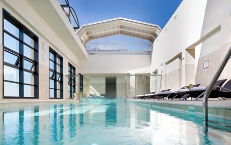 An indoor swimming pool with clear blue water, large windows, and sun loungers.