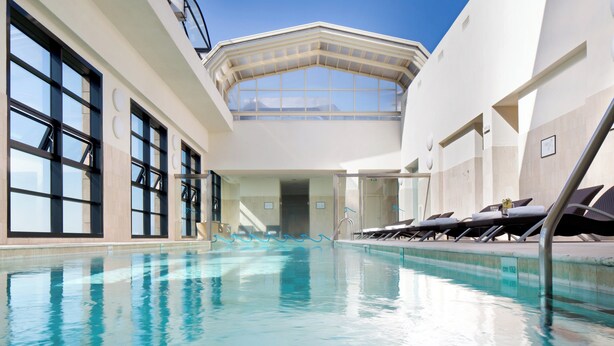 Una piscina interior con agua cristalina, ventanas amplias y tumbonas.