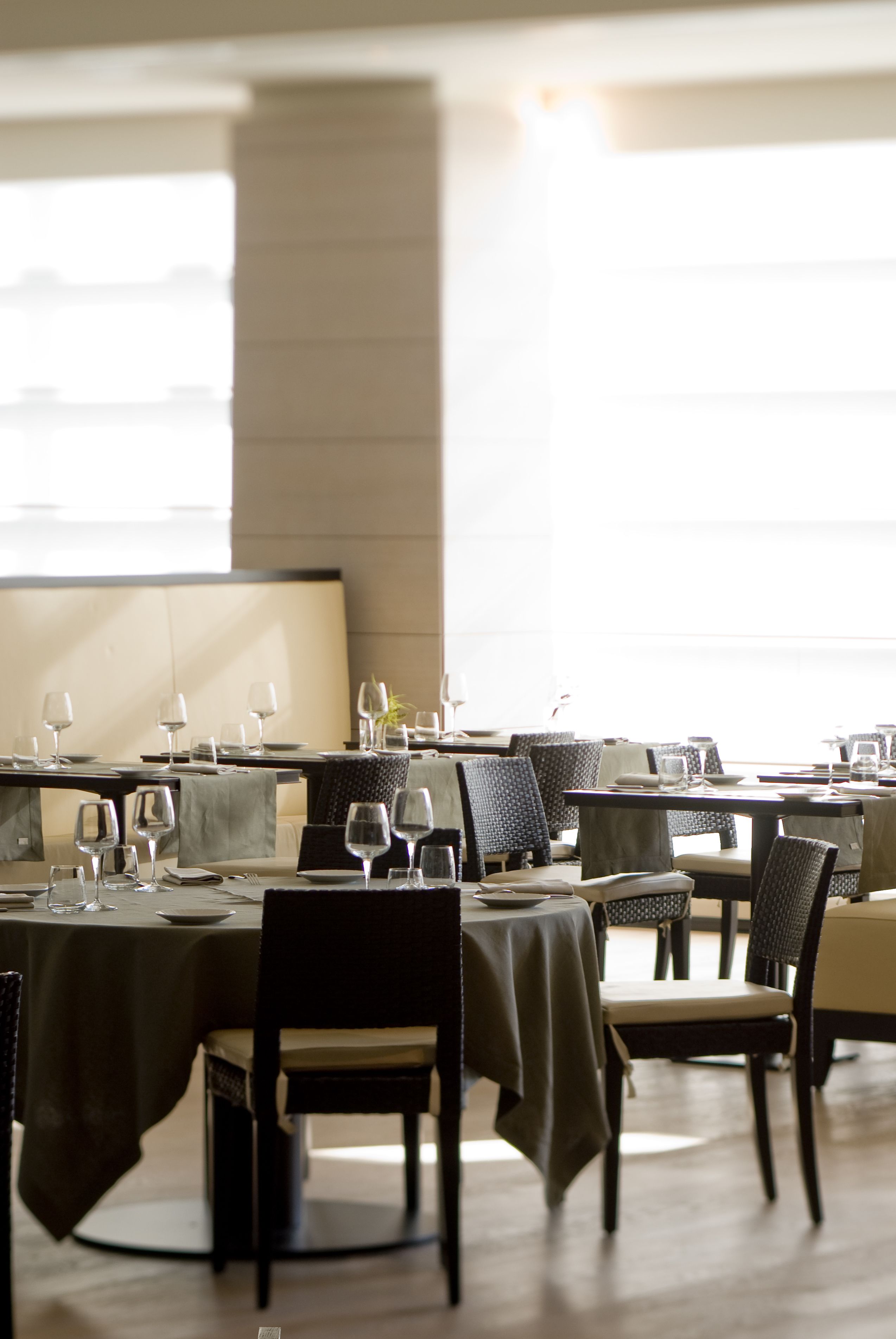 Ein Restaurant mit gedeckten Tischen, Stühlen und einem großen Fenster im Hintergrund.
