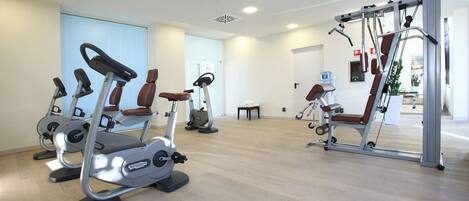 Uma academia com máquinas de cardio, um banco de musculação e um espelho.