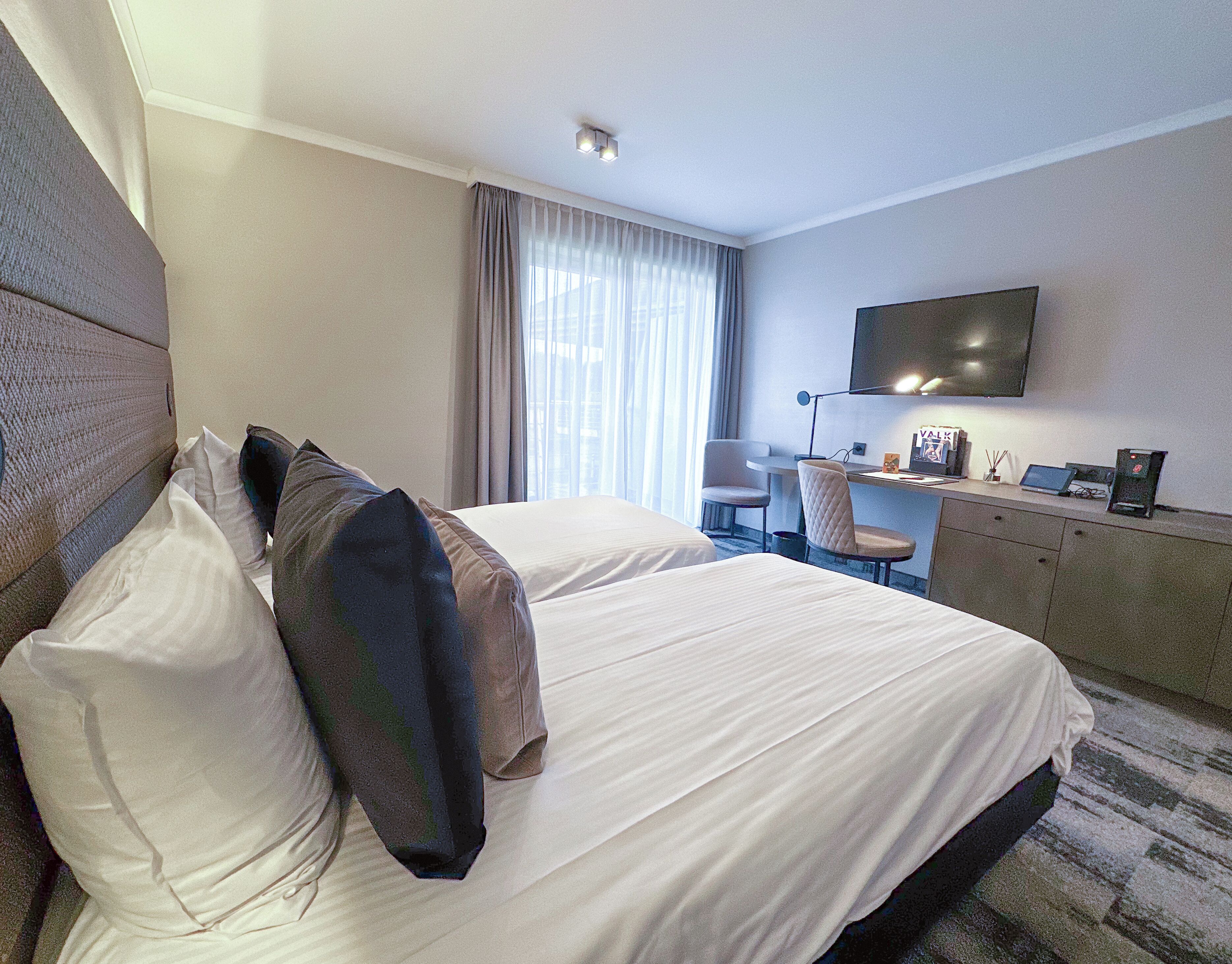 Una habitación de hotel con dos camas, un escritorio, una silla, un televisor y un minibar.