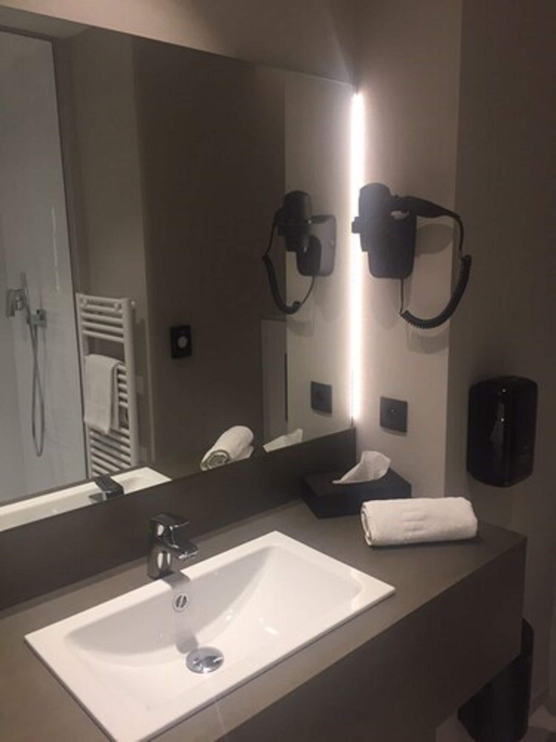 Een moderne badkamer met een grote spiegel, een wastafel, een handdoekhouder en een haardroger.