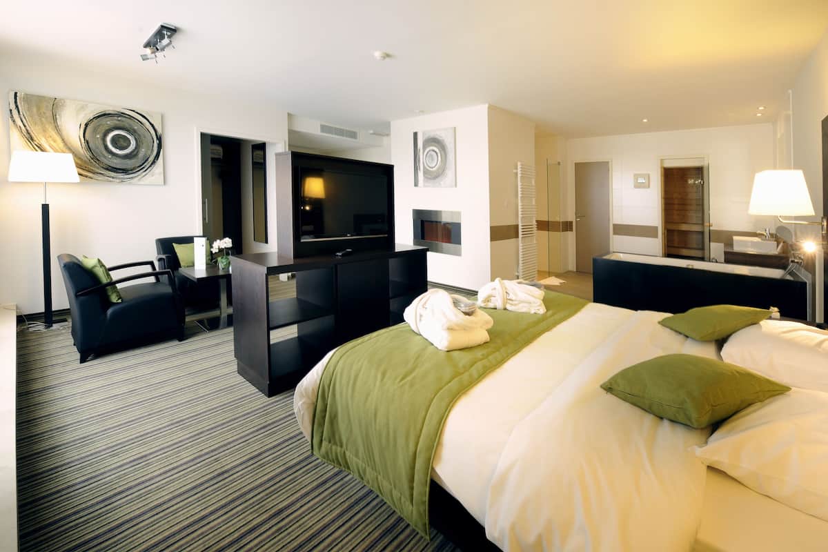 Ein Hotelzimmer mit einem großen Bett, einem Schreibtisch mit Stuhl, einem Fernseher und einem Badezimmer mit Waschbecken und Spiegel.