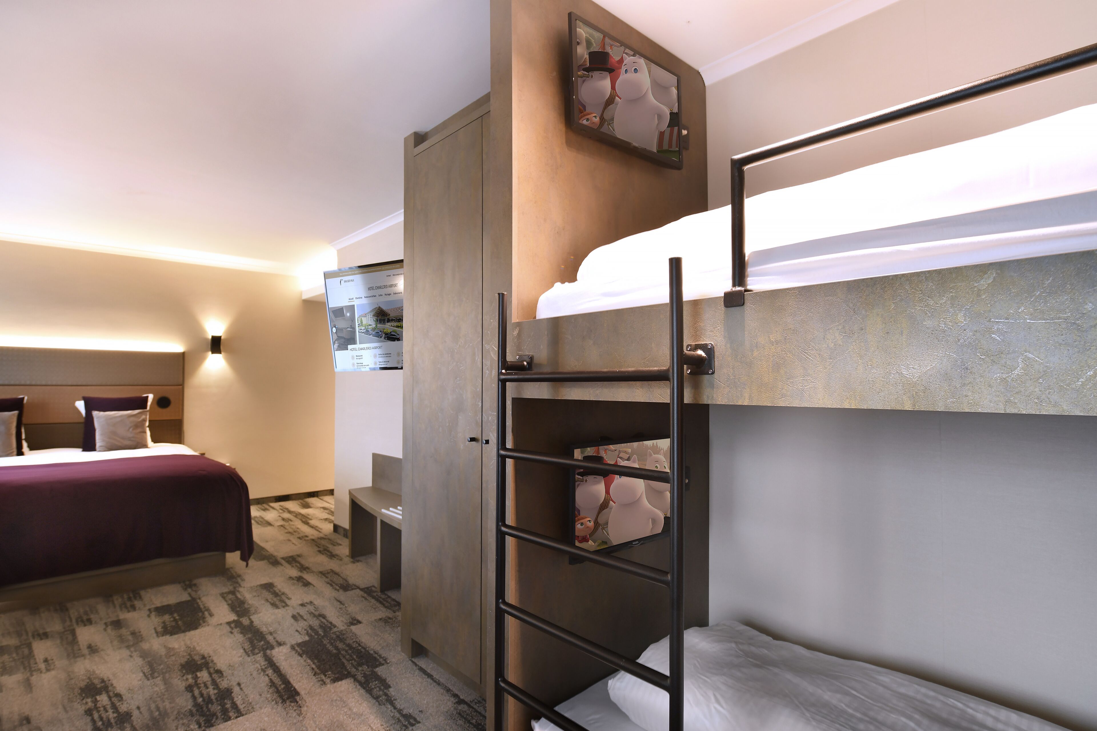 A hotel room with a bunk bed, a desk, and a wall-mounted TV.