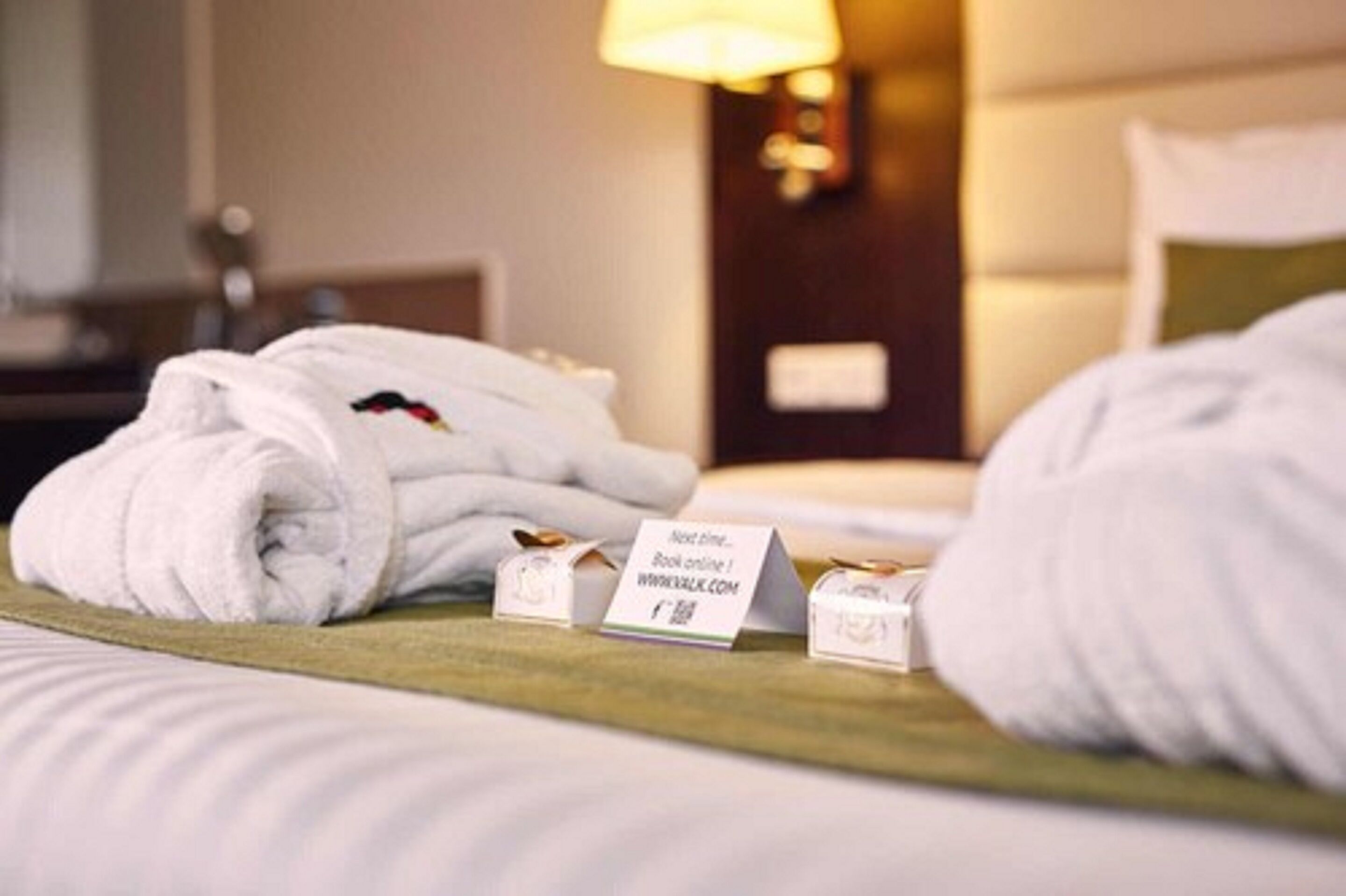 Una cama bien hecha con toallas blancas y un letrero que indica otra habitación.