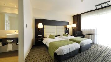 A hotel room with two beds, a large mirror, a bathroom with a sink, and a window with curtains.