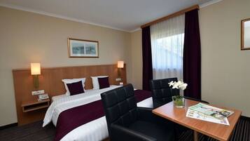 Une chambre d’hôtel avec un lit, deux chaises, une table et une fenêtre avec des rideaux.
